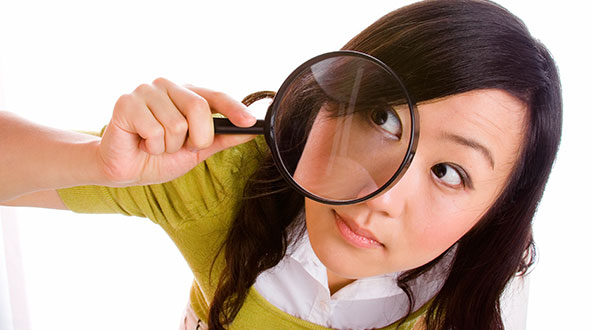 Asian girl with magnifying glass inspecting products